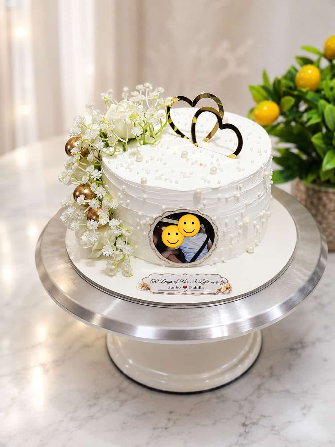White textured buttercream anniversary cake with pearl details, gold hearts, fresh white flowers and a circular edible photo print of a couple, personalised '100 Days of Us', by CakeCanva in Bahrain.