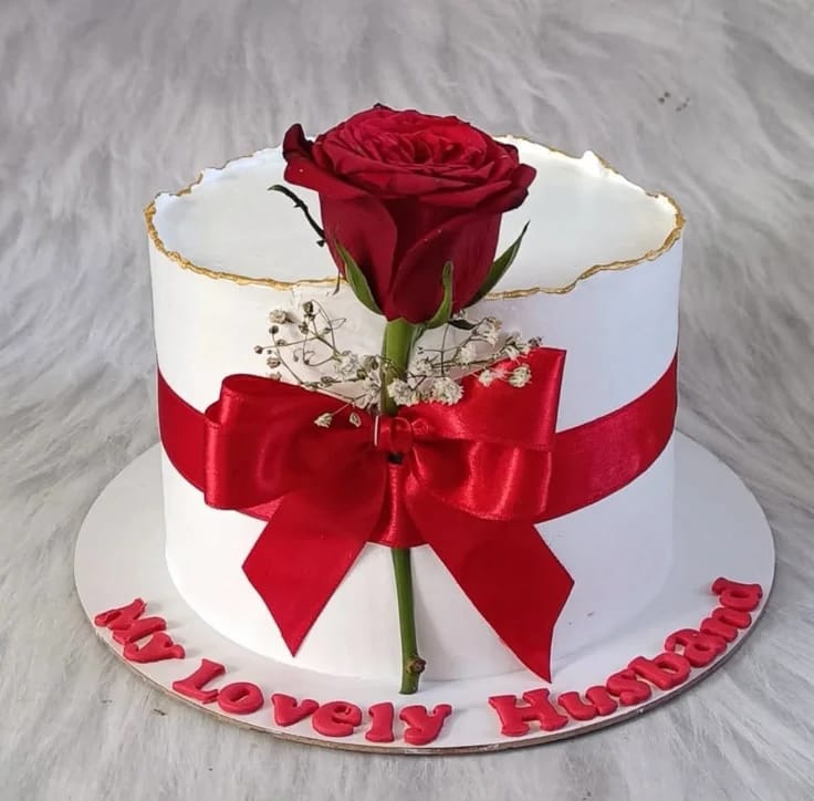 White anniversary cake topped with a single fresh red rose and a red satin ribbon, a popular flower theme cake choice in Bahrain.