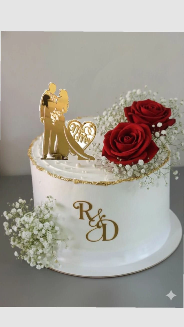 White wedding anniversary cake decorated with red roses, baby's breath, and a gold Mr and Mrs couple topper, ordered for couples in Bahrain.
