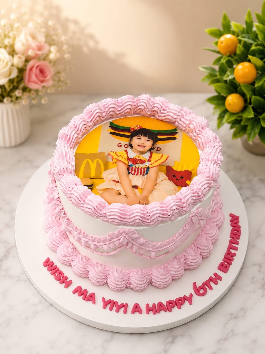Round cake with a pink piped shell border framing an edible photo print of a child in a McDonald's-themed outfit, personalized 'Wish Ma Yiyi a Happy 6th Birthday' in Bahrain.