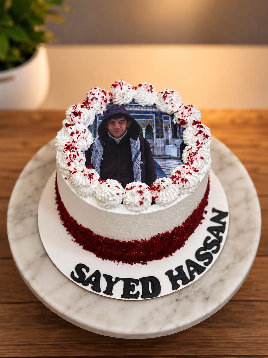 Red velvet crumb cake with whipped cream rosettes framing a personal photo of a young man, customized with the name Sayed Hassan for a Bahrain birthday.