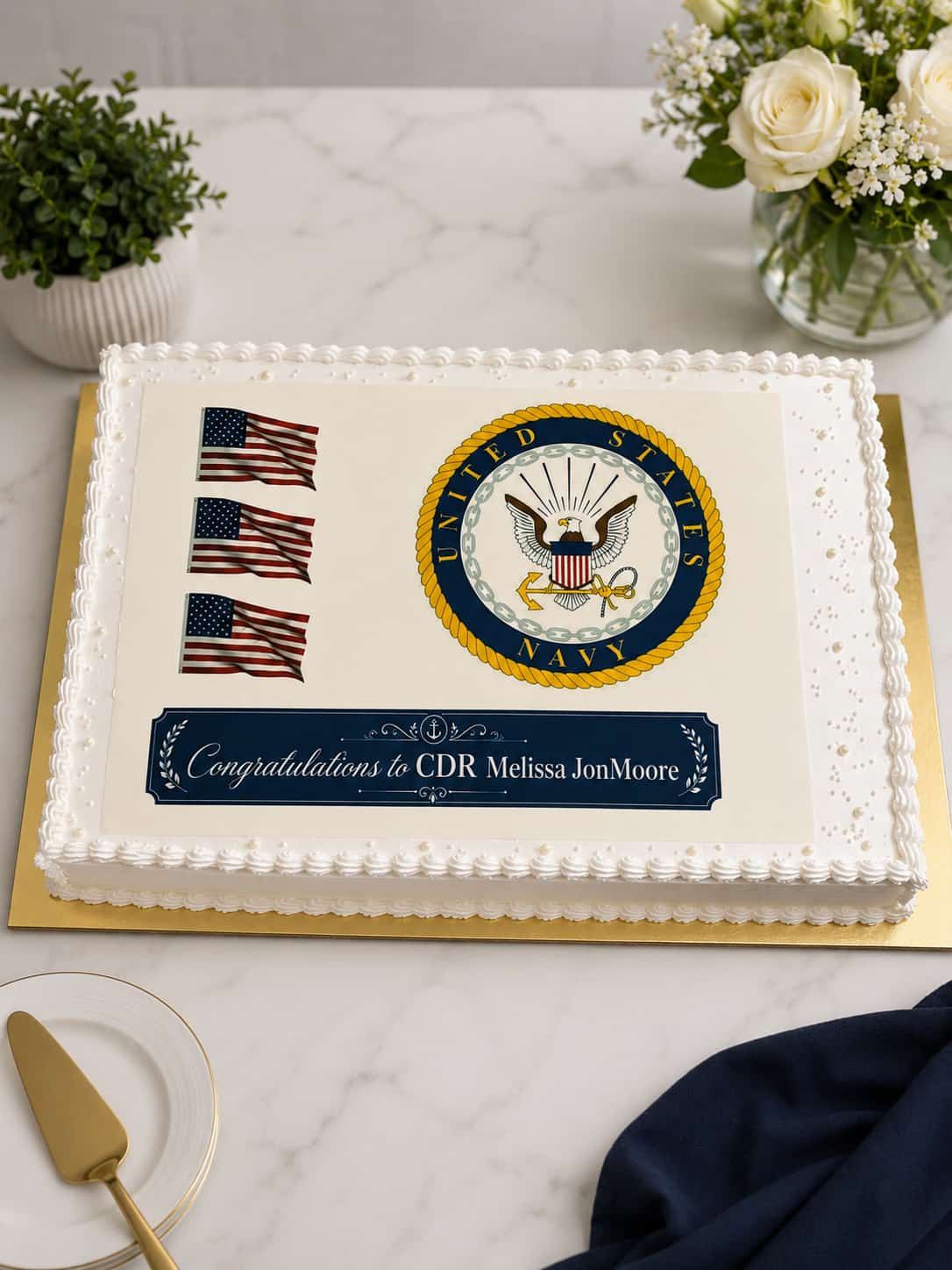 Rectangular white sheet cake with a pearl-dotted shell border and a full edible print of the United States Navy seal, three American flags and a 'Congratulations to CDR Melissa JonMoore' banner, in Bahrain.