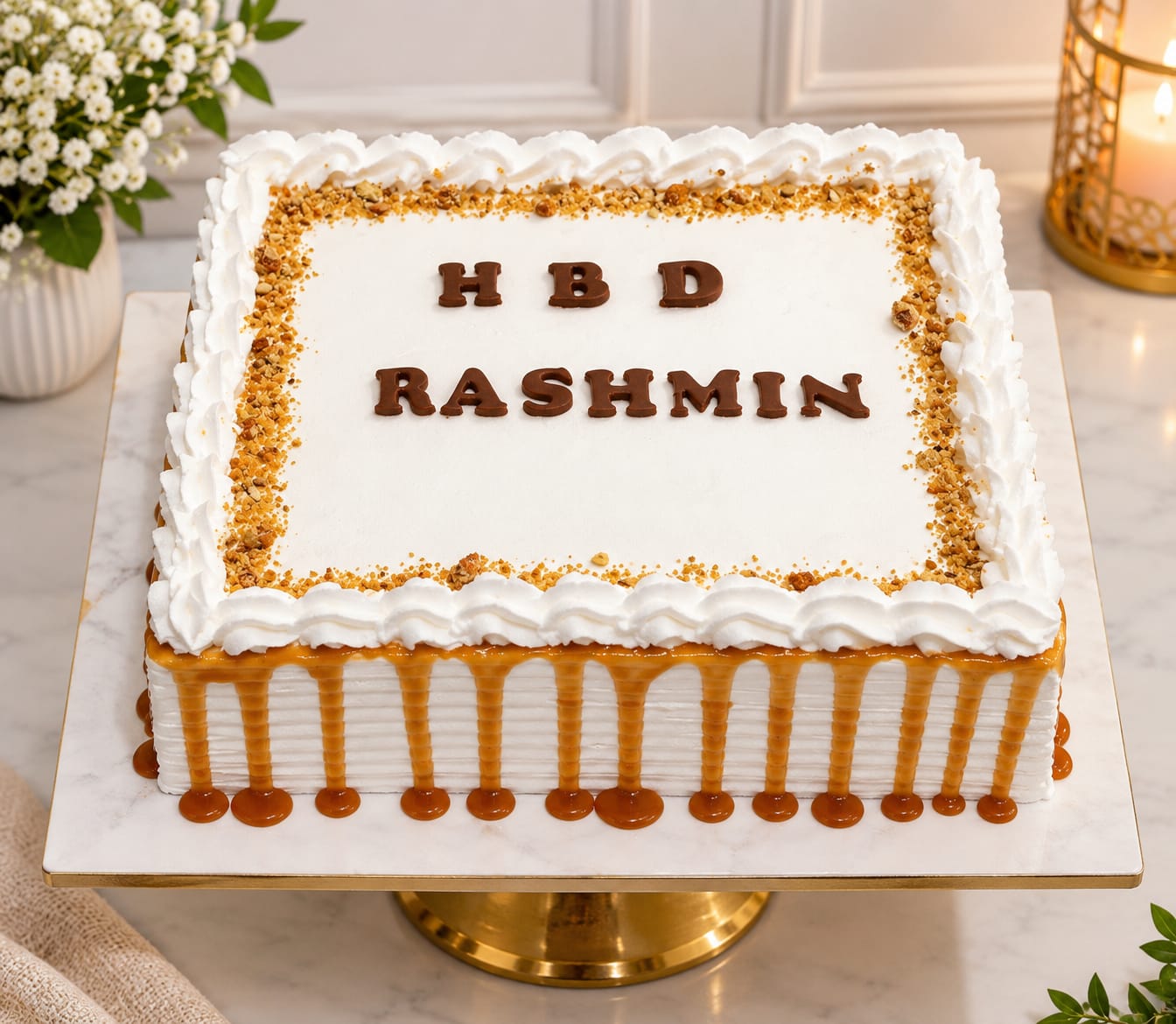 Square whipped cream cake with a crunchy butterscotch praline border, a golden caramel drip down the sides and 'HBD Rashmin' in chocolate letters, in Bahrain.