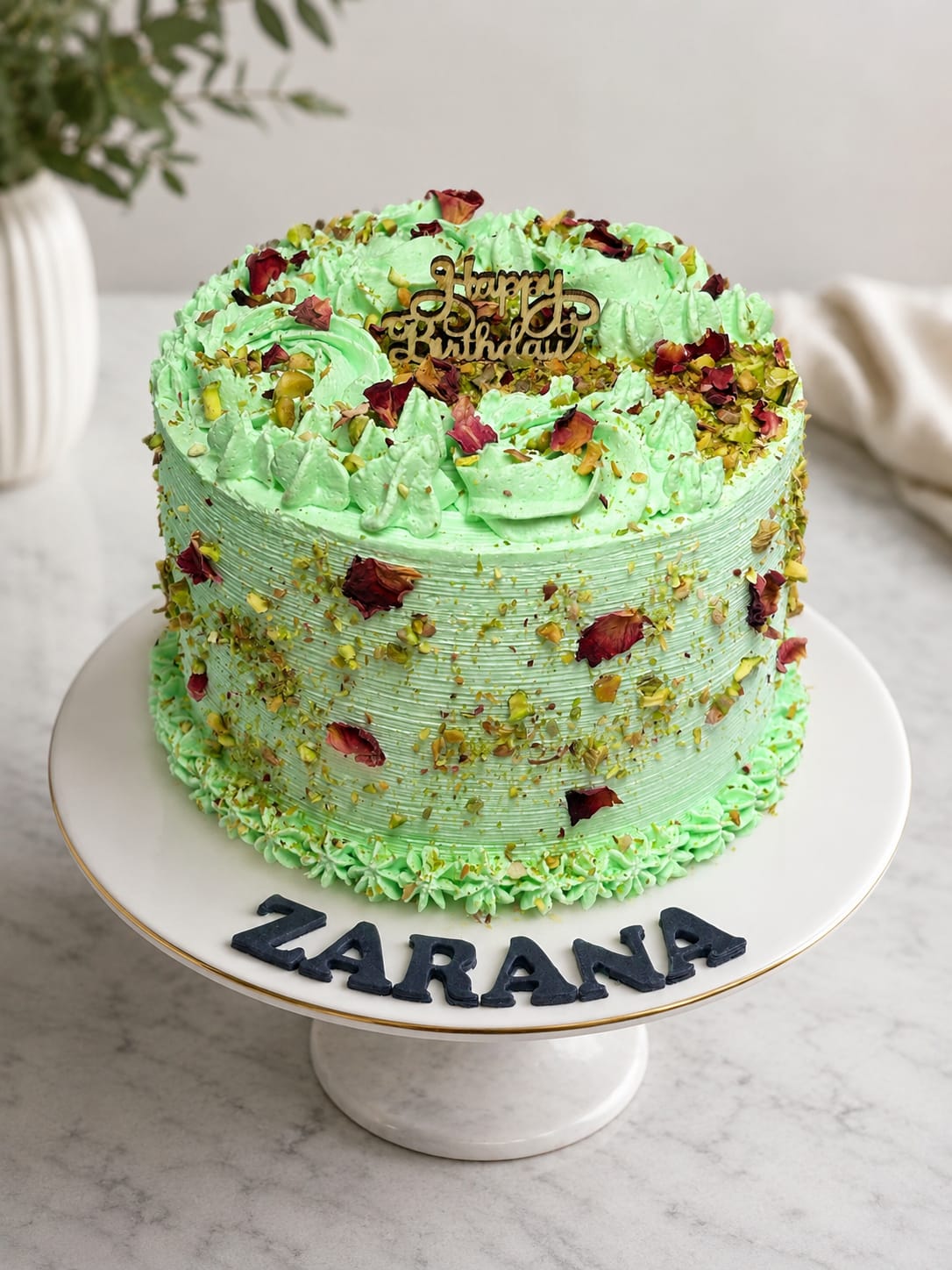 Green pistachio buttercream birthday cake topped with dried rose petals, crushed pistachios, and a gold Happy Birthday topper, a flower theme signature cake in Bahrain.