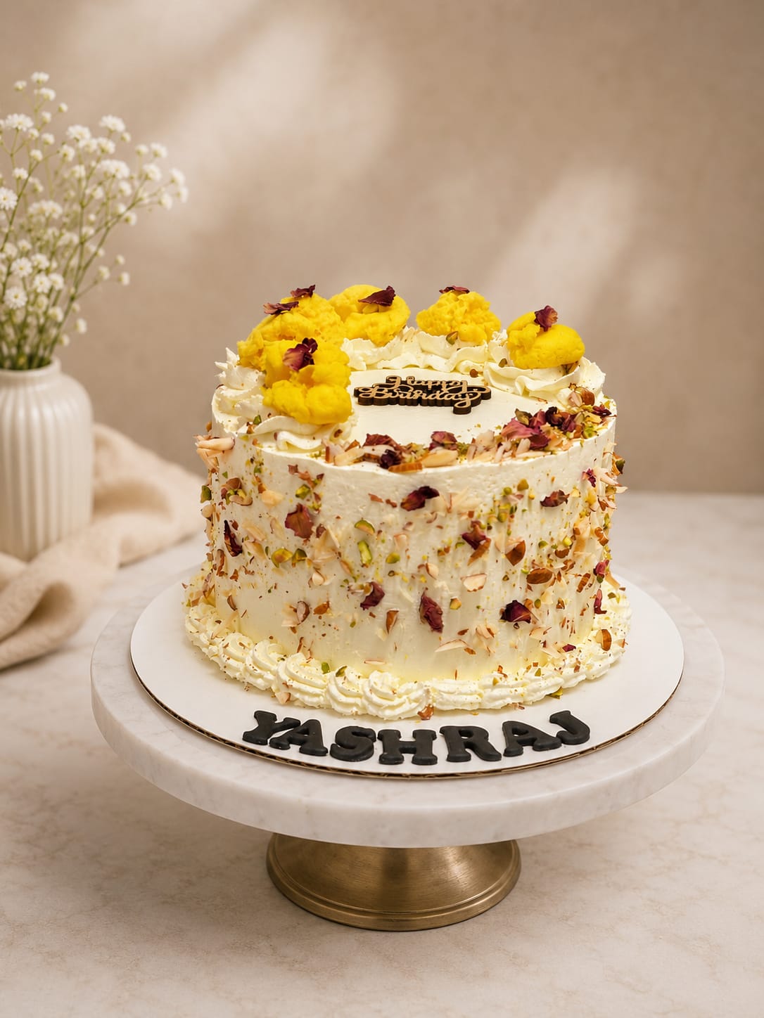 White birthday cake decorated with golden yellow buttercream rosettes, dried rose petals, and crushed pistachio and almond, a signature cake style in Bahrain.