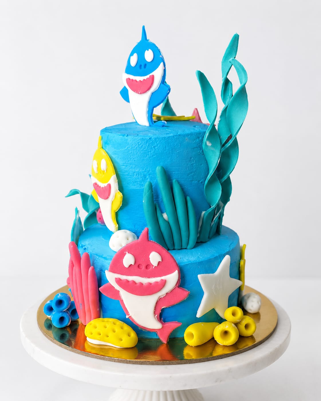 Two-tier blue ocean themed birthday cake decorated with Baby Shark family fondant figures, coral, and starfish, a custom theme cake in Bahrain.