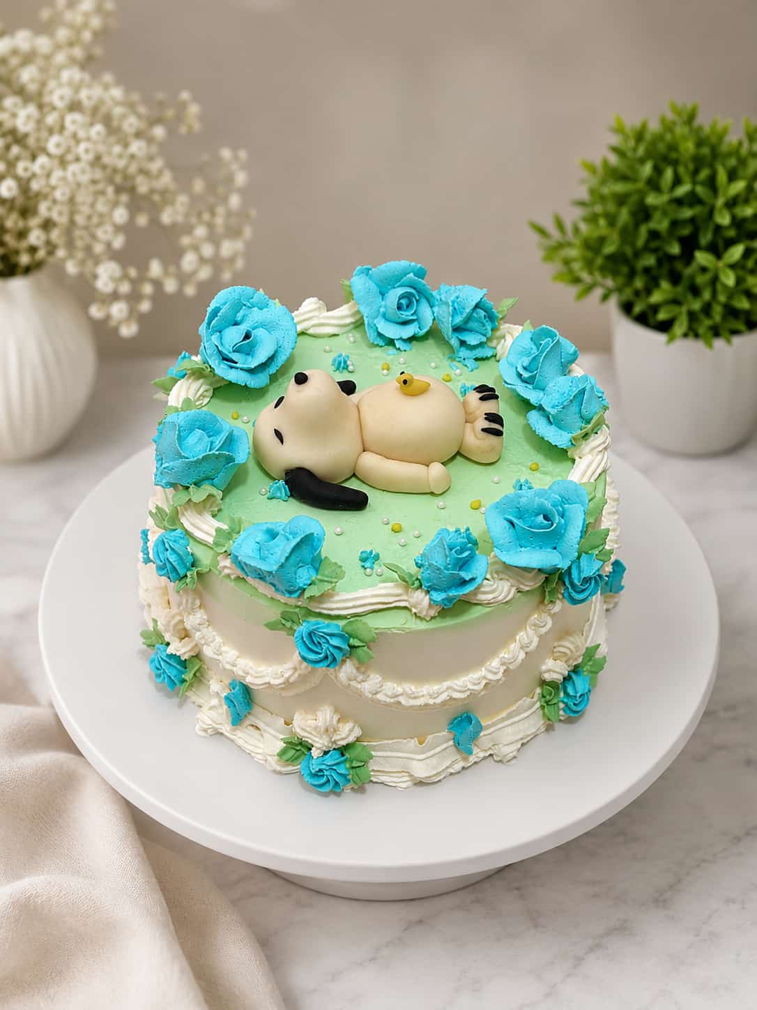Green buttercream cake topped with a fondant baby figure and rubber duck, bordered with turquoise piped roses and white lace draping, a baby shower theme cake in Bahrain.