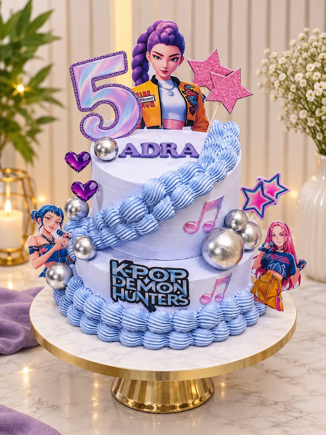 Two-tier lavender buttercream birthday cake with a blue piped braid, silver spheres, purple heart gems, character cutouts, pink star toppers and a holographic number 5, personalised 'Adra' with a K-Pop Demon Hunters plaque, in Bahrain.