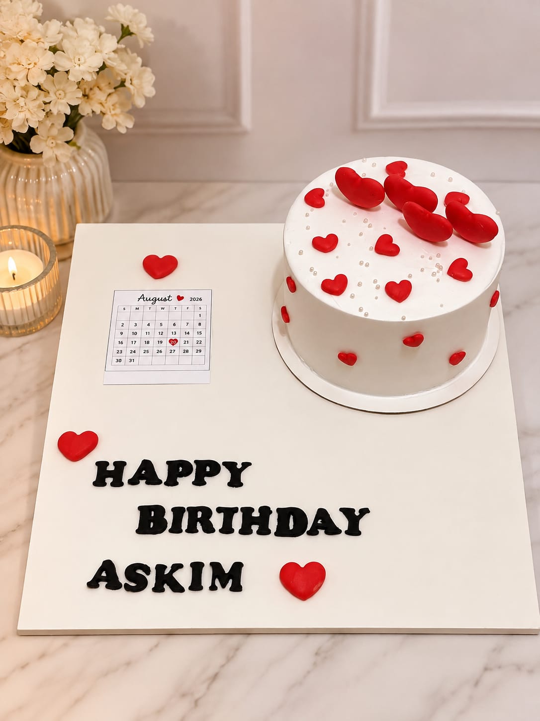 Simple white round cake scattered with red fondant hearts and white sugar pearls, presented on a board with 'Happy Birthday Askim' lettering, by CakeCanva in Bahrain.