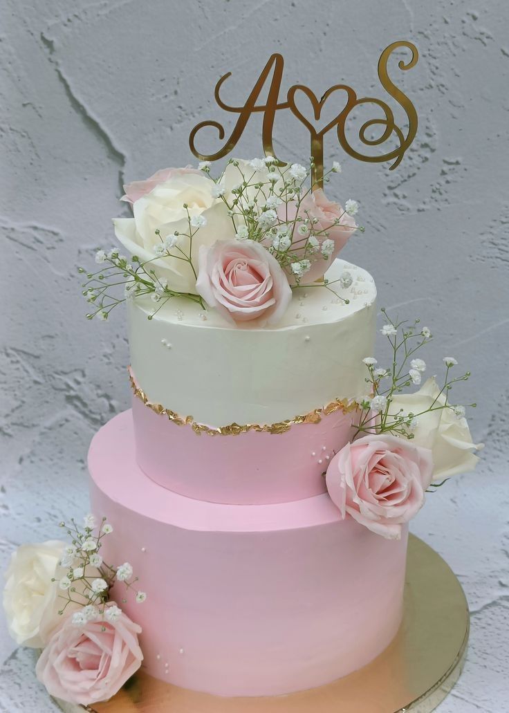 Two-tier blush pink ombre wedding cake finished with a gold leaf band, pink and white roses, and a gold monogram topper, a romantic wedding cake seen in Bahrain.
