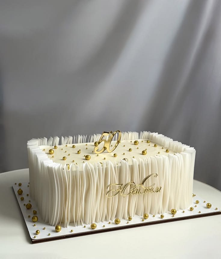 Square ivory fringe-textured cake decorated with gold pearls and a gold numeral topper, a striking wedding cake style available in Bahrain.