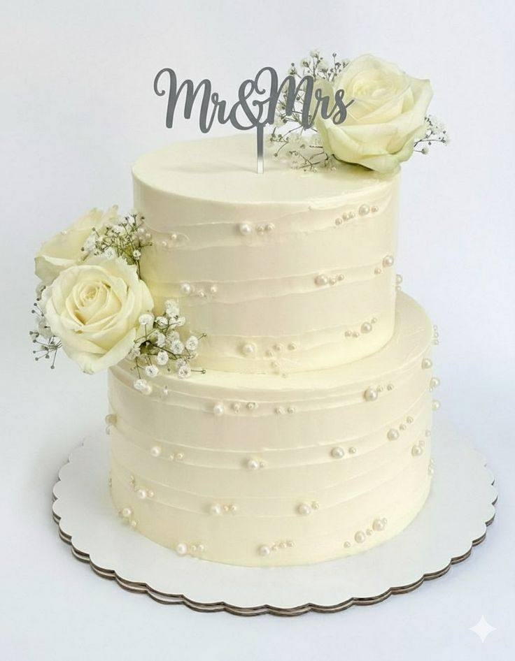 Two-tier ivory pearl-studded wedding cake topped with fresh white roses and a silver Mr and Mrs topper, a classic wedding cake style for Bahrain weddings.